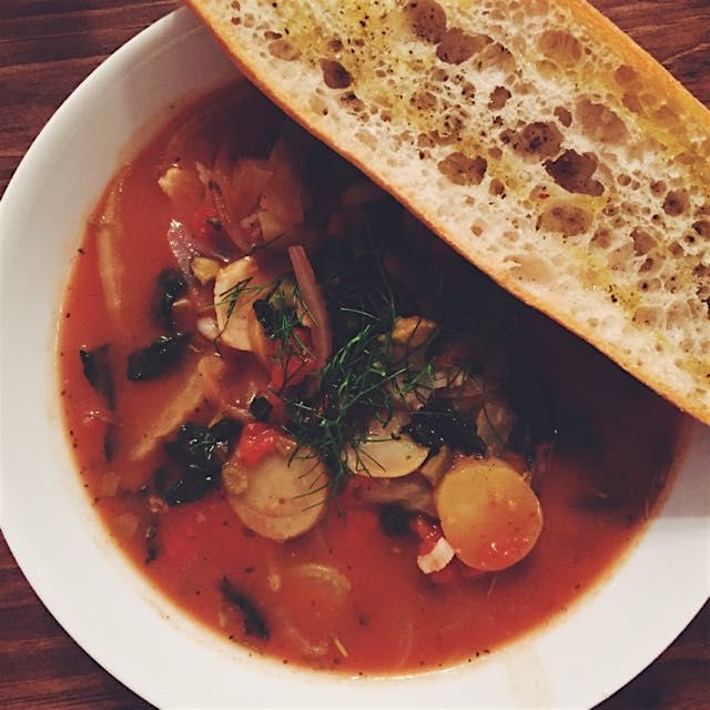 Bouillabaisse with kale, fennel, potatoes, olives, and cod. Crispy baguette on the side.
